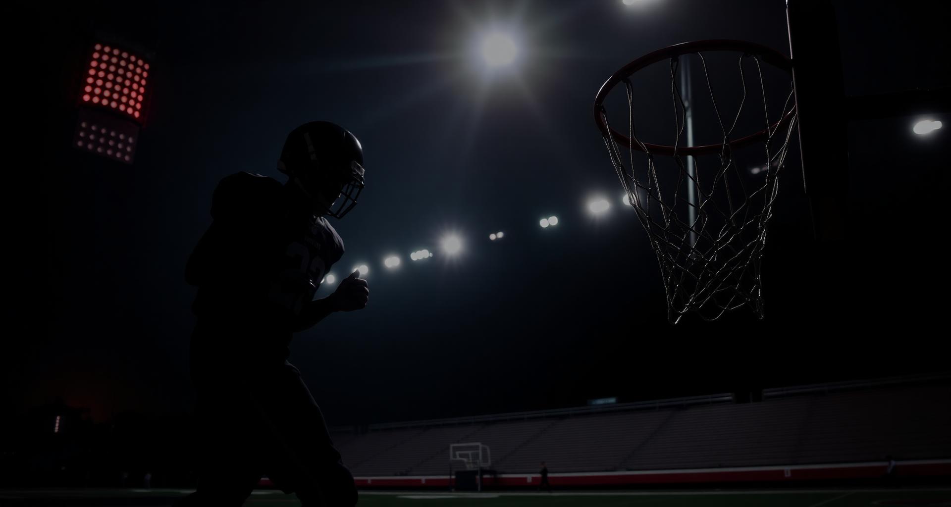 High school football player under stadium lights with basketball hoop